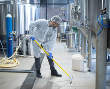 Professional industrial cleaner in protective uniform cleaning floor of food processing plant.